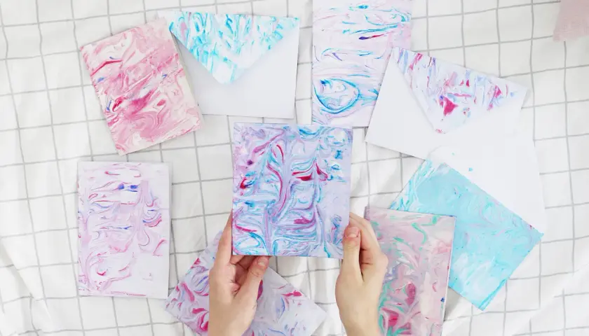Bunte Karten und Umschläge mit Marmorierungsmuster, die an fließendes Wasser erinnern. Papier marmorieren ist eine kreative Technik.