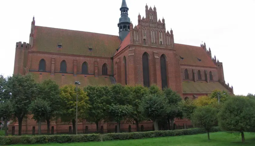 Gotycka katedra w Pelplinie, ceglana budowla z charakterystyczną wieżą i strzelistymi oknami, otoczona zielenią.