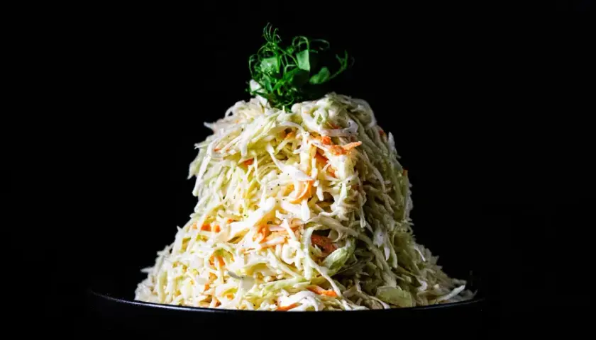 Ein Berg aus Krautsalat mit Karotten, verfeinert mit cremigem coleslaw dressing, gekrönt von grünen Sprossen.