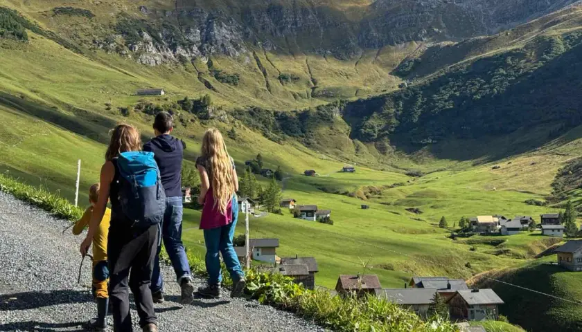 Familie genießt das Liechtenstein wandern in den Alpen. Grüne Hänge, kleine Häuser und ein majestätischer Berg im Hintergrund.
