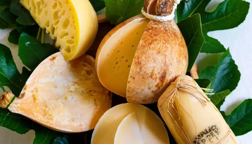 Varietà di formaggio caciocavallo, alcuni interi, altri tagliati, su foglie verdi.