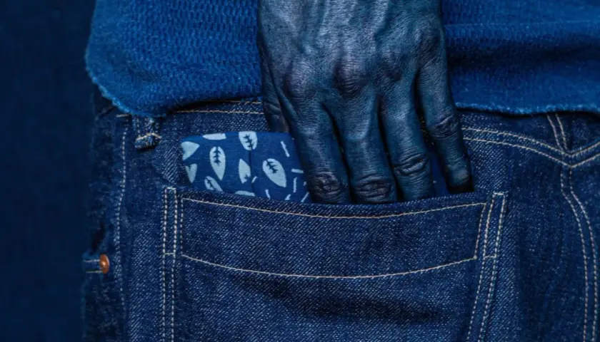Main bleue, main plongée dans la poche d'un jean, le tissu orné de feuilles, témoignage de la teinture.