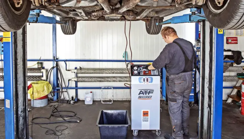 Mechanik wykonuje dynamiczną wymianę oleju w skrzyni biegów za pomocą specjalistycznego urządzenia.