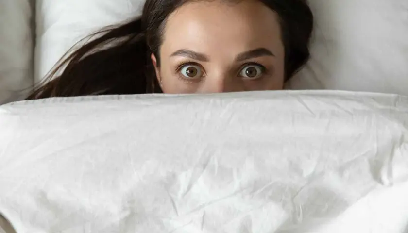 Occhi spalancati sotto le coperte, un'espressione di pura paura di dormire.