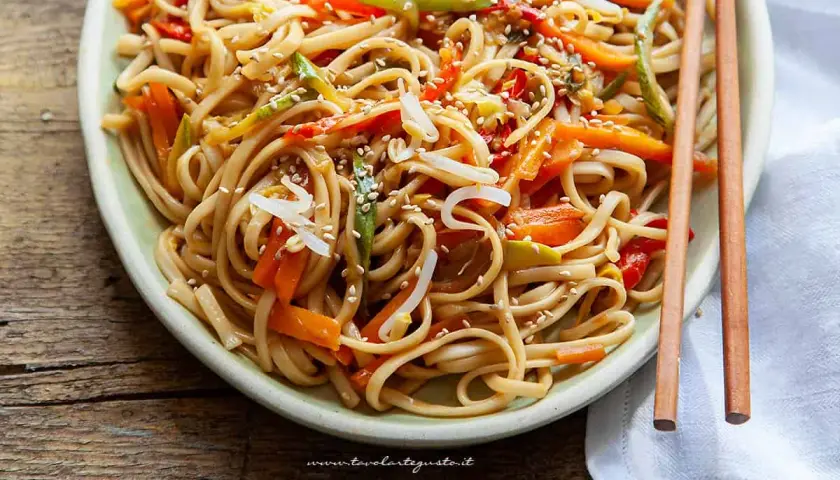 Noodles con verdure colorate, carote, peperoni e germogli di soia, guarniti con semi di sesamo.