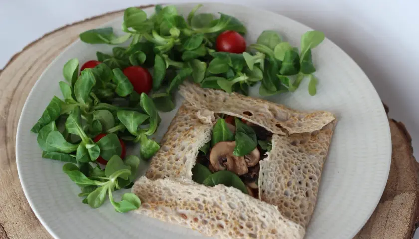 Une galette bretonne garnie de champignons et d'épinards, accompagnée d'une salade verte et de tomates cerises. Un délice pour accompagner un verre de vin.