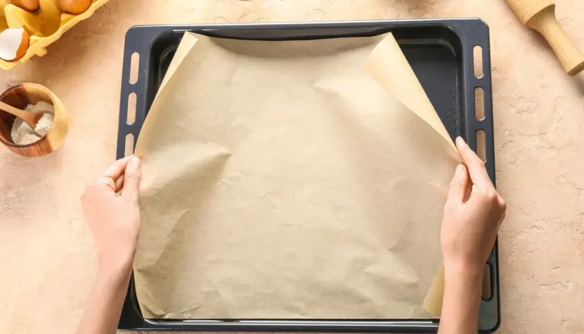 Dłonie układają papier do pieczenia na blasze.