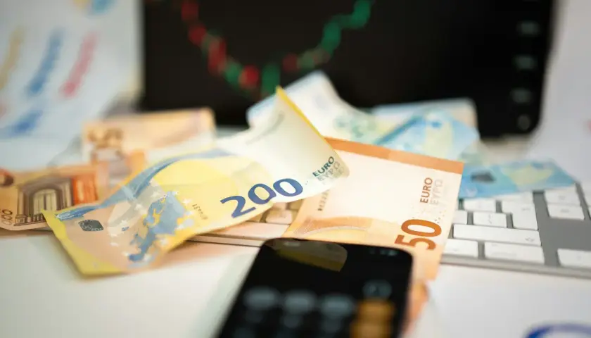 Euro banknoty na klawiaturze, telefon i wykres giełdowy sugerują, jak inwestować w waluty.
