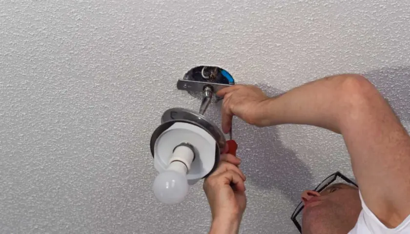 Un homme effectue le branchement d'une lampe au plafond, utilisant un tournevis pour fixer le luminaire.