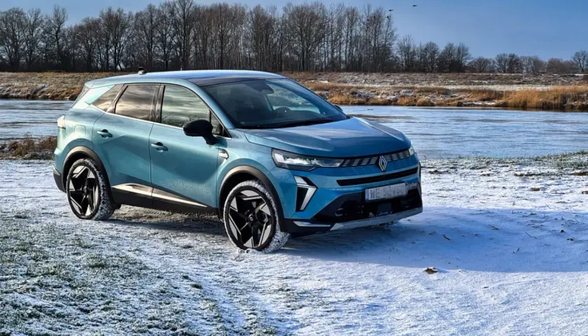 Niebieski Renault Symbioz zaparkowany na zaśnieżonej polanie nad zamarzniętą rzeką.