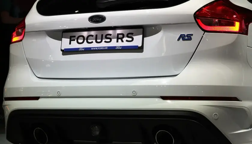 Biały Ford Focus RS z niebieskim znaczkiem RS i podwójnymi końcówkami wydechu.