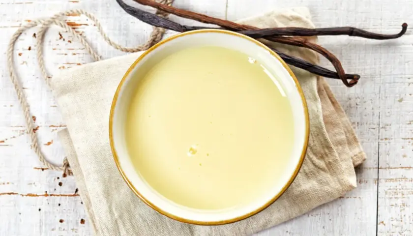 Un bol de crème anglaise onctueuse, prêt à être dégusté, avec des gousses de vanille à proximité.