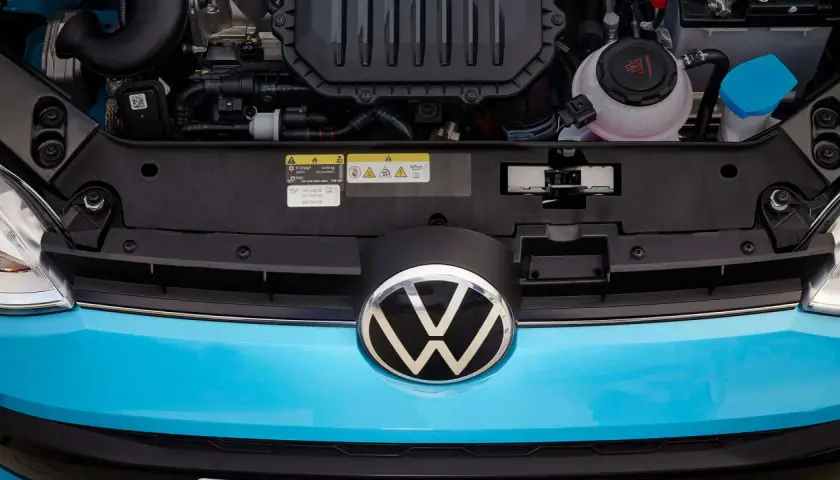 Motorutrymmet på en blå Volkswagen. En etikett visar information om olja och kylvätska, vilket kan vara relevant vid ett **volkswagen gasbil problem**.