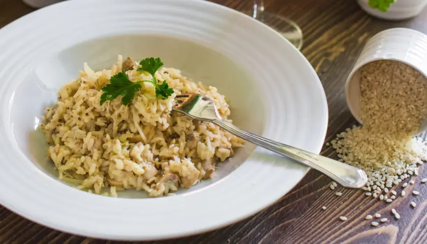 Un cremoso risotto con champiñones y queso parmesano, listo para disfrutar. Al lado, un cuenco volcado con arroz para risotto.