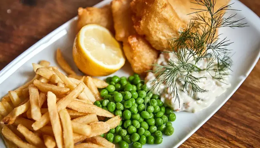 En tallrik med fish and chips, ärtor, citronklyfta och remouladsås.