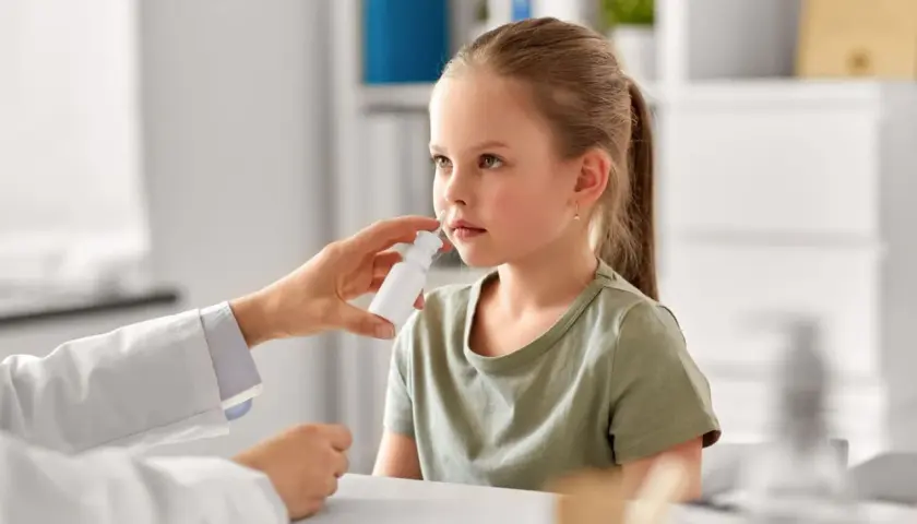 Niña recibe spray nasal para aliviar síntomas de rinitis alérgica. El doctor investiga las causas.