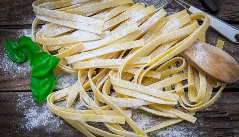 Świeży makaron tagliatelle posypany mąką, z listkami bazylii i drewnianą łyżką.
