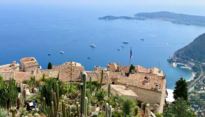 Ein malerischer Blick auf die **Côte d'Azur** mit einem Kakteengarten, alten Häusern und dem azurblauen Meer voller Yachten.