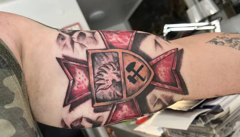 Tatuaż patriotyczny na ramieniu: lew w koronie i skrzyżowane młot i kilof na tle czerwonej gwiazdy.
