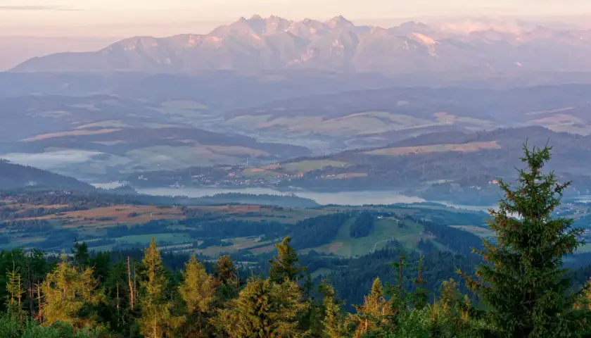 Widok z lubań szczyt na Tatry o wschodzie słońca. Mgły unoszą się nad doliną, a lasy i pola tworzą malowniczy krajobraz.