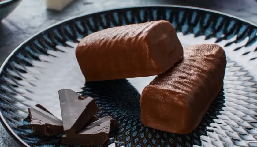 Dwa czekoladowe batony proteinowe na talerzu z kawałkami gorzkiej czekolady. Idealne do domowego przepisu na batony proteinowe.