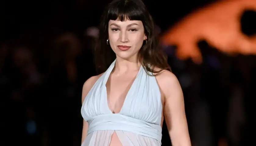 Mujer con flequillo vasco y vestido vaporoso azul claro, posando con mirada directa.