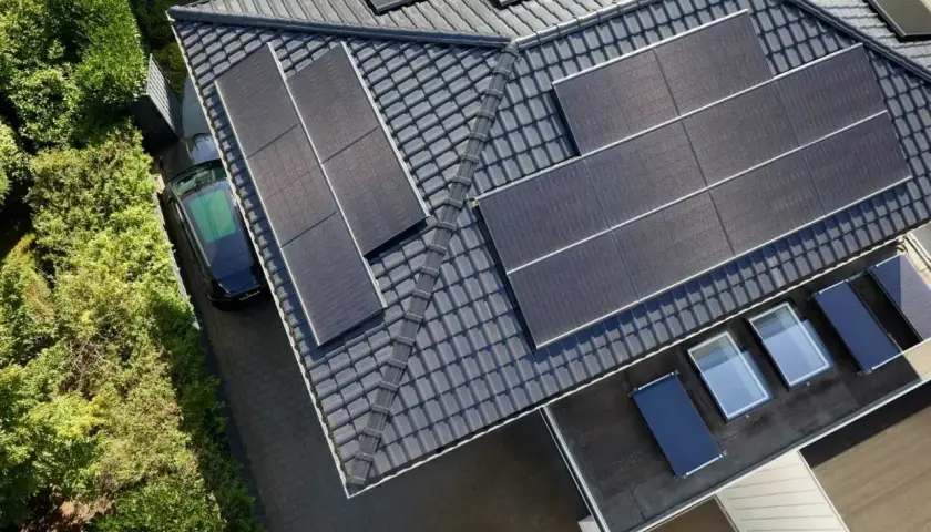 Dach mit Solarmodulen, ein schwarzes Auto und grüne Bäume. Die **agri pv voraussetzungen** sind erfüllt für dieses sonnenbeschienene Haus.