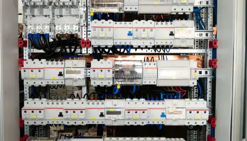 Wnętrze rozdzielni elektrycznej z licznymi wyłącznikami, bezpiecznikami i przewodami.