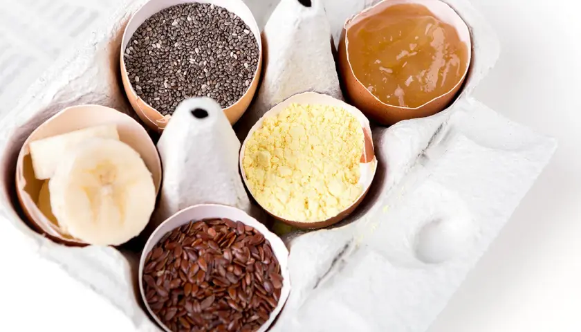 Dans une boîte à œufs, des alternatives pour remplacer les œufs : graines de chia, compote de pommes, farine de pois chiche, graines de lin, rondelles de banane.