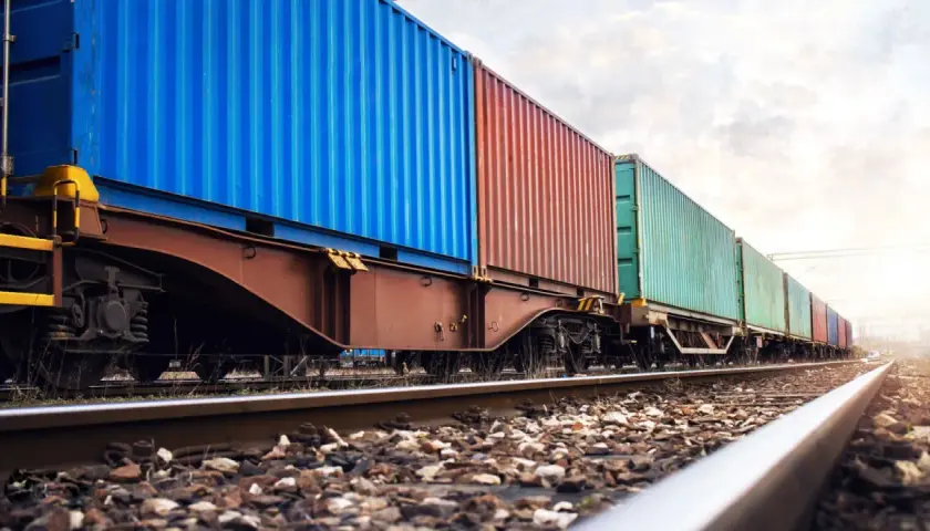 Długi pociąg towarowy z kolorowymi kontenerami na torach. To przykład transportu kolejowego, który jest kluczowy dla globalnej logistyki.