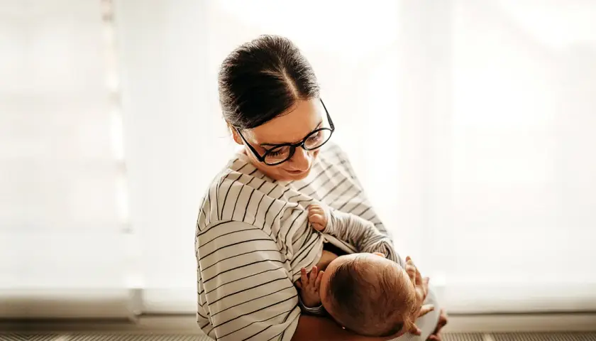 Matka karmi piersią dziecko, które już nie ulewa. Delikatny uścisk, spojrzenie pełne miłości.