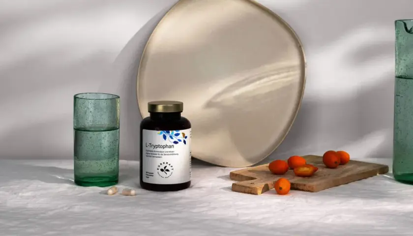 Flasche L-Tryptophan, die Vorstufe für Serotonin, neben Gläsern und Kumquats.