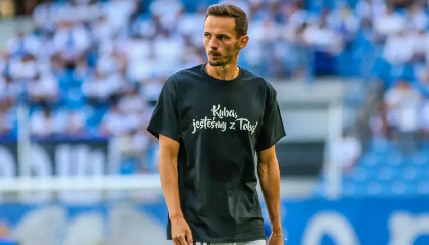 Rafał Wolski, komentator, na boisku w koszulce "Kuba, jesteśmy z Tobą!".