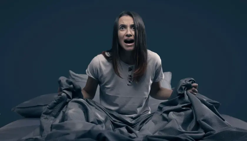 Mujer en la cama, con expresión de angustia, sujetando las sábanas. Parece que se despierta sobresaltada porque me encuentro mal por las mañanas.