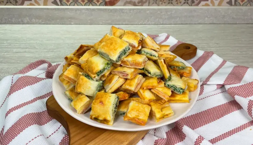 Un mucchio di salatini con pasta sfoglia, alcuni ripieni di spinaci e altri di prosciutto, pronti per essere gustati.