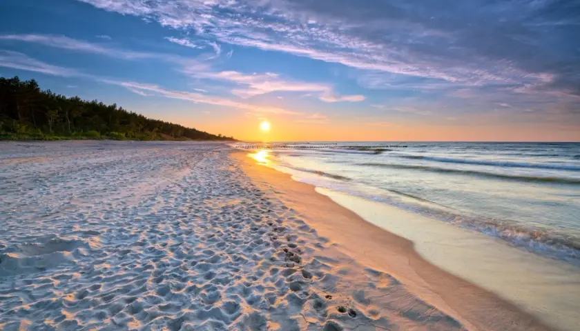 Zachód słońca nad morzem, piaszczysta plaża z odciskami stóp, las w tle. Idealne, fajne miejsce nad morzem dla dwojga na romantyczny spacer.
