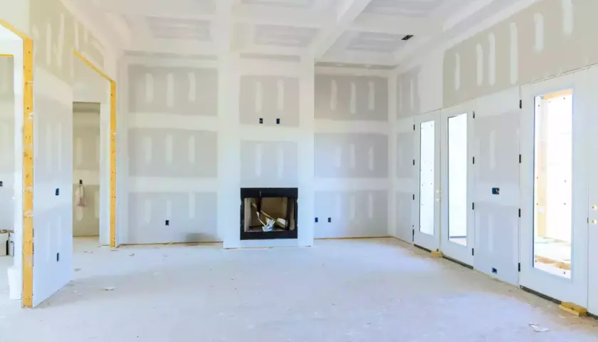 Interno di una casa in costruzione con pareti e soffitti rifiniti con rivestimento in cartongesso, camino e porte a doppio battente.