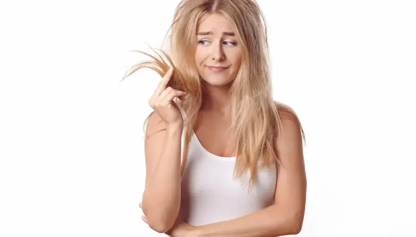 Mujer rubia con pelo poroso y enredado, tocándose un mechón con expresión de preocupación.