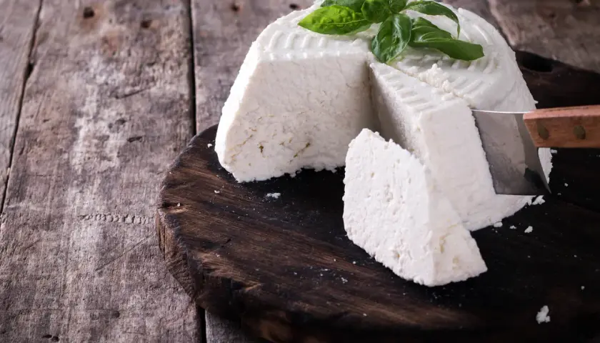 Ricotta fatta in casa, fresca e profumata, guarnita con basilico, pronta per essere gustata su un tagliere di legno rustico.