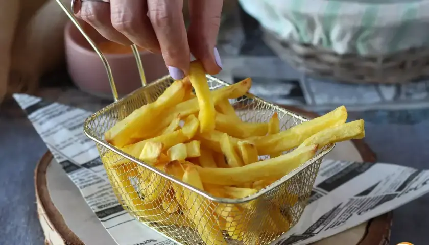 En hand plockar upp en gyllene pommes frites ur ett korgfat. Perfekt för en snabb aptitretare.