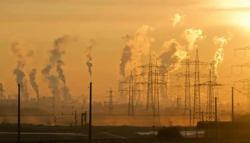 Dymiące kominy fabryk i linie energetyczne na tle zachodzącego słońca. To obraz przemysłowego krajobrazu, który ilustruje przyczyny zmian klimatu.