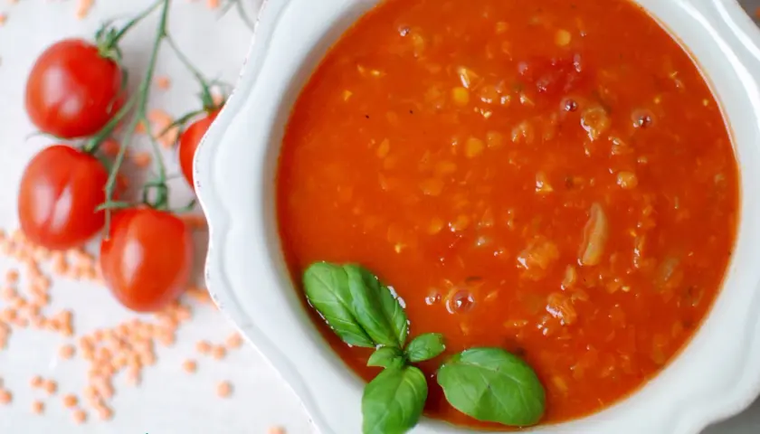 Zupa pomidorowa z soczewicą, ozdobiona bazylią. Obok gałązka pomidorków i rozsypana soczewica. Idealna na chłodne dni, smakuje jak domowe pesto pomidorowe.