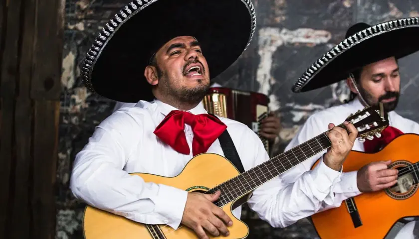 Muzycy mariachi w sombrero i białych koszulach z czerwonymi muszkami grają na gitarach.
