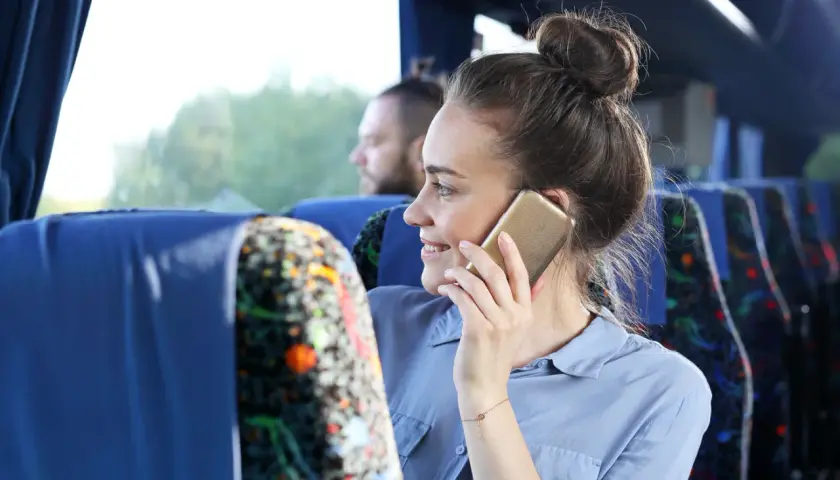Kobieta w autobusie rozmawia przez telefon, zastanawiając się, jak włączyć roaming w Plus.