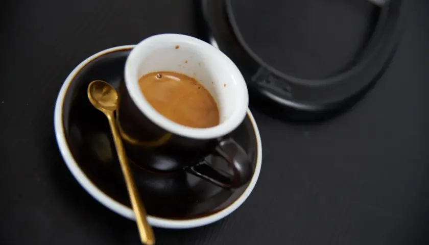 Aromatyczne włoskie espresso w filiżance z złotą łyżeczką na czarnym tle. Idealny początek dnia.