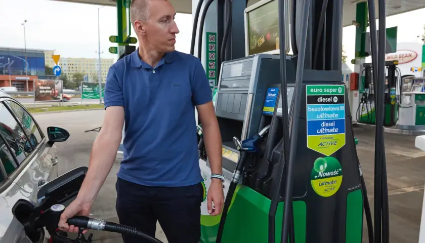 Mężczyzna tankuje samochód, pokazując, jak zatankować auto. Widoczna jest dystrybutor paliwa z różnymi rodzajami paliwa.