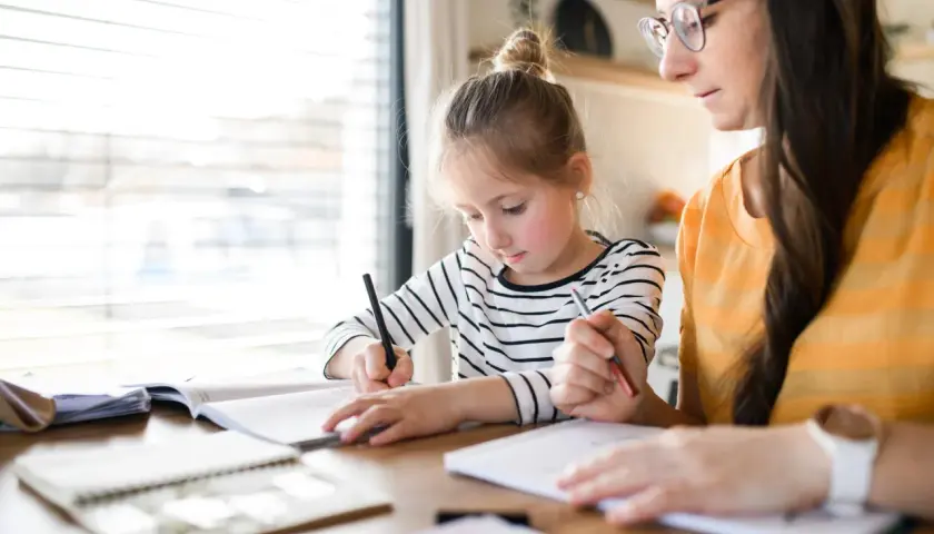 Dziewczynka z mamą uczą się w domu. Jak zacząć edukację domową? Skupienie na nauce i wsparcie rodziców.