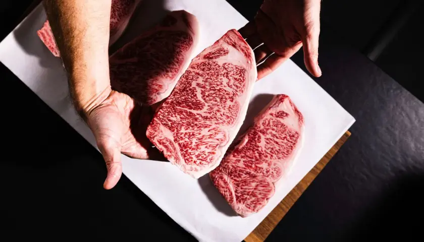 Des mains présentent des steaks de bœuf persillés, marbrés de gras, promettant le meilleur bœuf du monde.