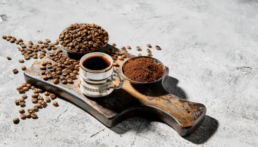 Chicco di caffè, macinato e bevanda scura su tagliere rustico. Chi dice che il caffè fa male, non ha visto questa meraviglia.