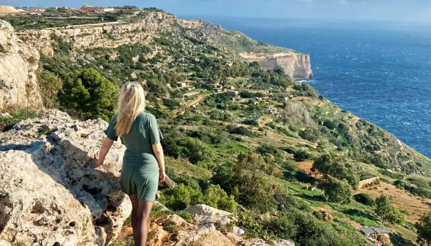 Malta, luty. Pogoda słoneczna, wietrzna. Kobieta na klifie podziwia widok na morze i zielone wzgórza.